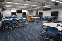 View of room with lectern on centered and projection screens and markerboards located on side walls 