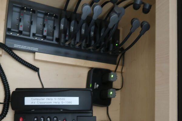 Pedestal - inside view of drawer showing two wireless mics in charging base and assistive listening devices in charger