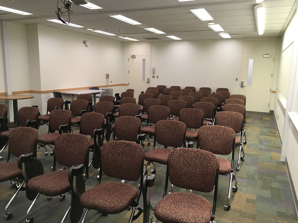 Photo of back of room from front of room with tablet armchairs on casters and doors at back.