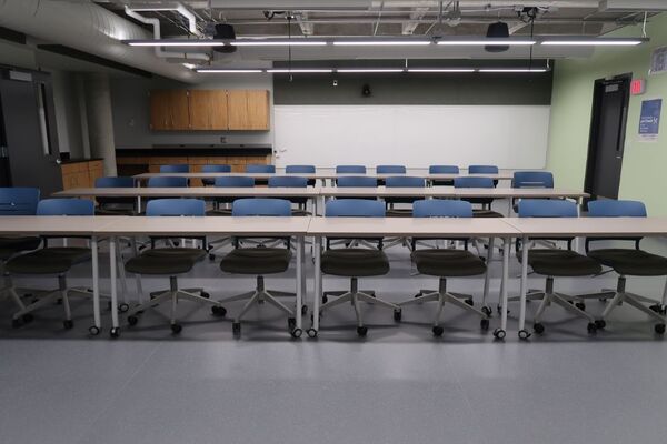 Back of room view of student table and chair seating and an exit door at rear right of room