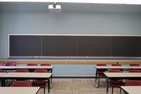 Rear of room view of student table and chair seating with chalkboard at rear of room