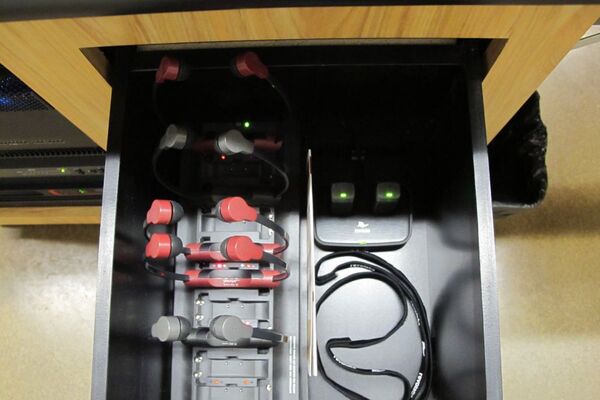 Pedestal - inside view of drawer showing two wireless mics in charging base and assistive listening devices in charger