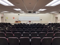 Front of room view with lectern on left in front of markerboard and exit doors on left and right