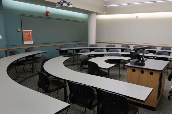 Back of room view of student tiered fixed-table and chair seating and tackboard on back wall