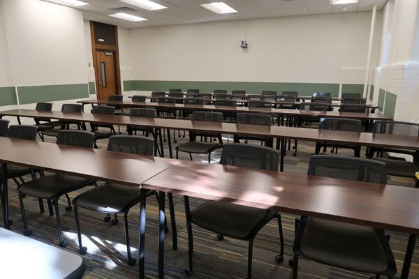 Back of room view of student table and chair seating and exit door at rear left of room