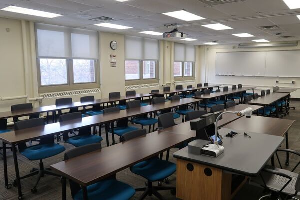 Back of room view of student table and chair seating and side markerboard on right wall of room