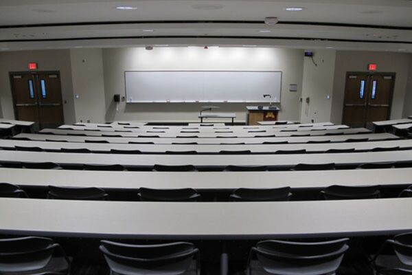 Front of room view with lectern on right in front of markerboard, exit doors on left and right of markerboard