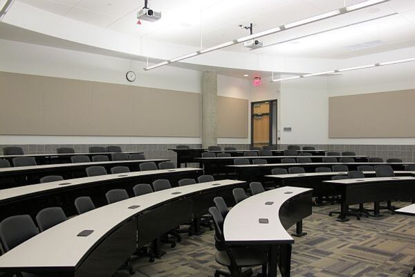 Back of room view of student tiered fixed -table and chair seating and exit door at right rear of room
