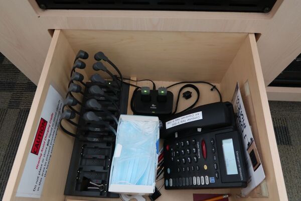 Pedestal - inside view of drawer showing two wireless mics in charging base, telephone, and assistive listening devices in charger