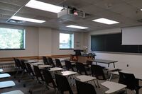 Front of room view with lectern on left in front of chalkboard and projection screen partially raised