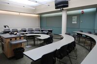 Back of room view of student tiered fixed-table and chair seating and confidence monitor on wall above