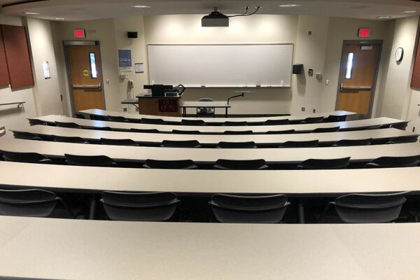 Front of room view with lectern on left in front of markerboard and exit doors on left and right of markerboard