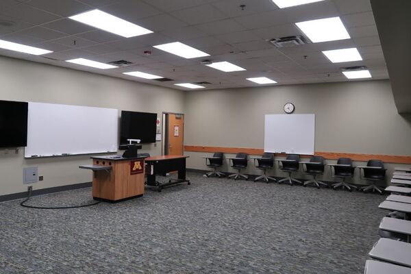 Front of room view with lectern on left in markerboard and display monitors to the left and right
