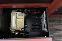 Pedestal - inside view of drawer showing two wireless mics in charging base, assistive listening devices in charger, and telephone
