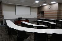 Front of room view with lectern center in front of markerboard and projection screen lowered with exit door at front right