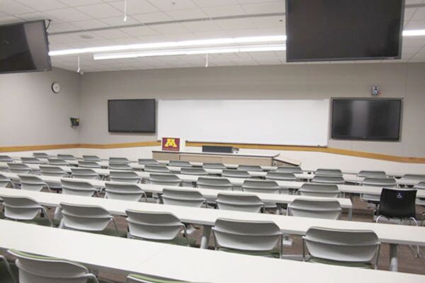 Front of room view with lectern center in front of markerboard and display screens to left and right