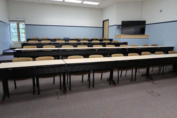 Back of room view of student tiered table and chair seating and display monitor on right rear wall