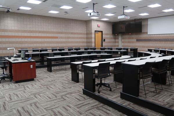 Back of room view of student tiered fixed-table and chair seating and  exit door at rear of room