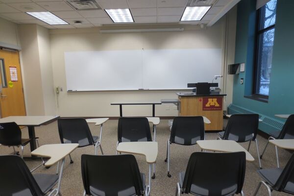 Front of room view with lectern on right in front of markerboard and exit door on the left
