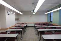 Rear of room view of student table and chair seating with clock at left side of room