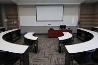 Front of room view with lectern center in front of markerboard and projection screen lowered 