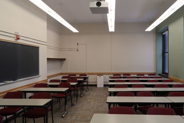 Rear of room view of student table and chair seating and chalkboard on left side of room
