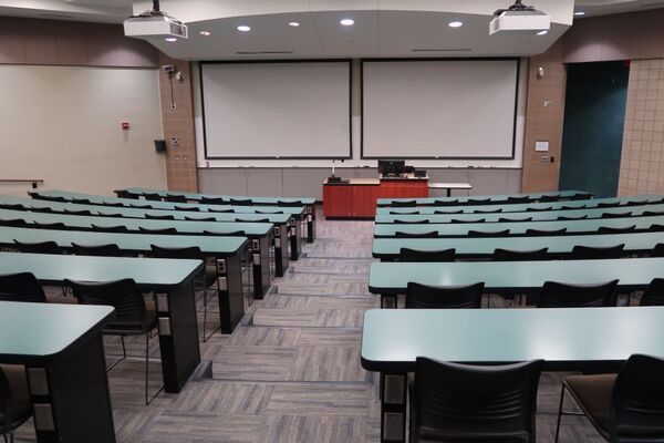 Front of room view with lectern center in front of markerboard and dual projection screens lowered