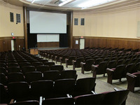Front of room view with lectern on left in front of stage and projection screen partially raised